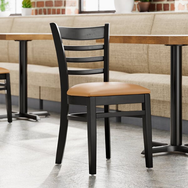 A Lancaster Table & Seating wood ladder back chair with a light brown vinyl seat next to a table in a restaurant dining area.