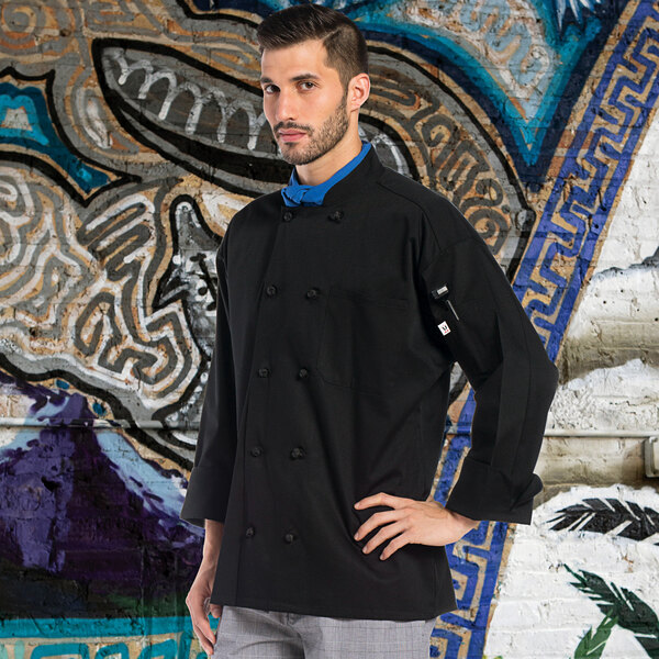 A man wearing a black Uncommon Chef long sleeve chef coat standing in front of a mural.