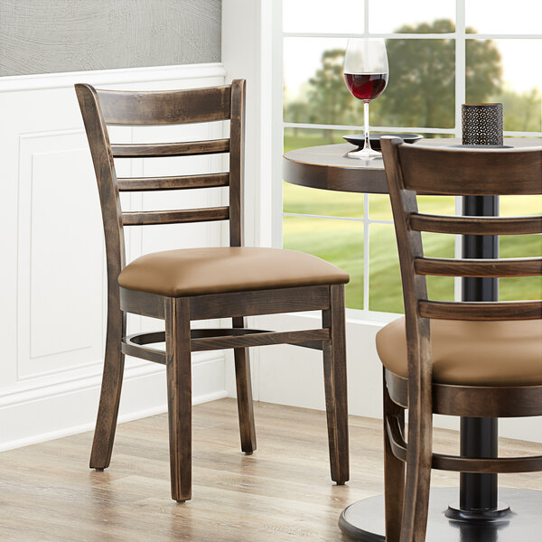 A Lancaster Table & Seating wood ladder back chair with a light brown cushion on a table in a restaurant dining area.