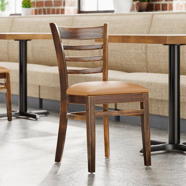 A Lancaster Table & Seating wood ladder back chair with a light brown cushion on a table in a restaurant.