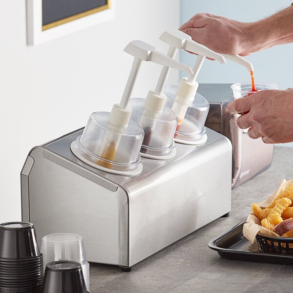 A person using a Steril-Sil stainless steel condiment dispenser to pour liquid into a cup on a counter.