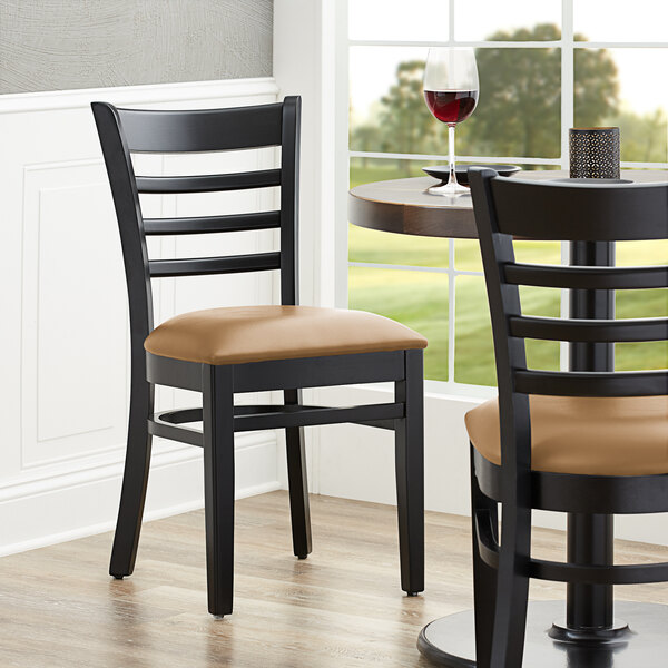 A Lancaster Table & Seating black wood ladder back chair with a light brown vinyl seat on a table in a restaurant.