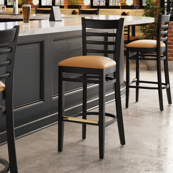 A Lancaster Table & Seating black wood bar stool with a light brown cushion on the seat.