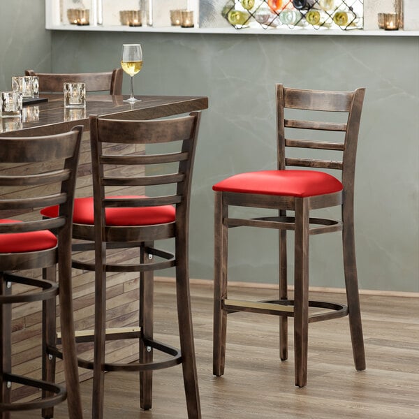 A Lancaster Table & Seating wood ladder back bar stool with a detached red vinyl seat.