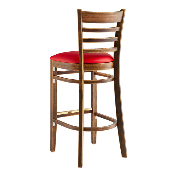 A Lancaster Table & Seating wooden bar stool with red vinyl seat sitting on a table.