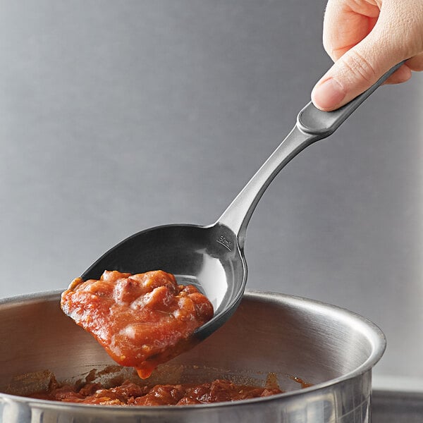 A person using a Linden Sweden Gourmaid high-heat nylon prep spoon to pour food into a pot.