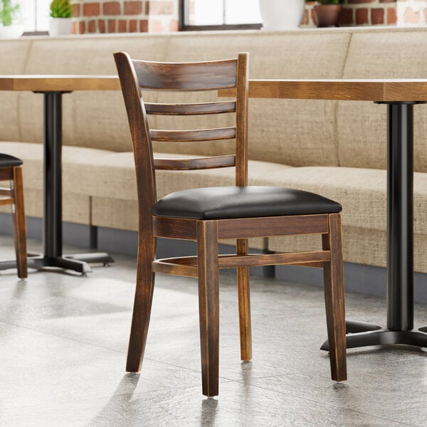 A Lancaster Table & Seating wooden ladder back chair with a black vinyl seat.