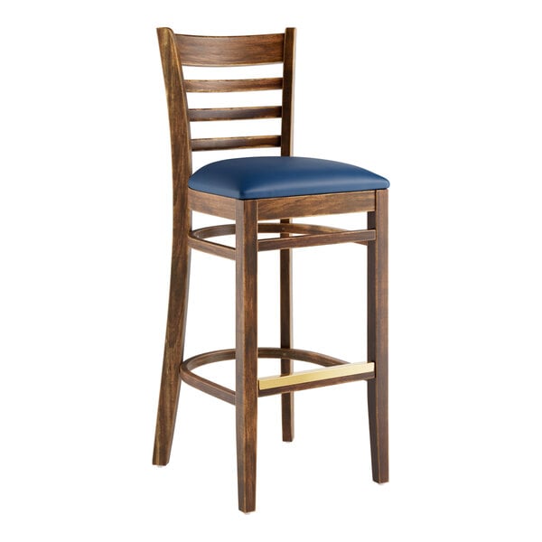 A Lancaster Table & Seating wooden ladder back bar stool with a navy vinyl seat.