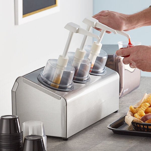 A person pouring sauce into a Steril-Sil stainless steel condiment dispenser.