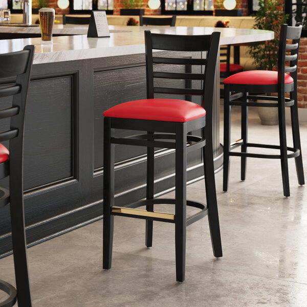 A Lancaster Table & Seating black wood bar stool with red vinyl seat.