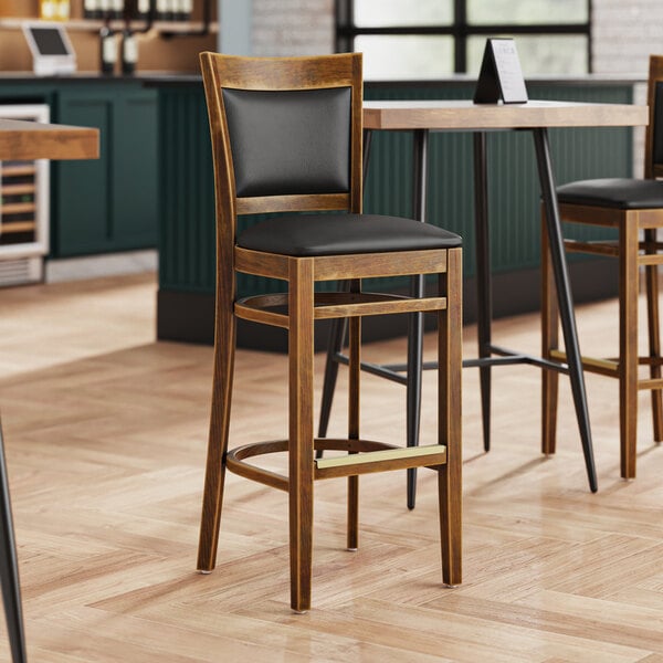 A Lancaster Table & Seating Sofia wood bar stool with black vinyl seat.