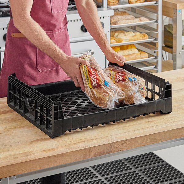 A man holding a black Orbis bakery bread tray with a plastic bag of bread inside.