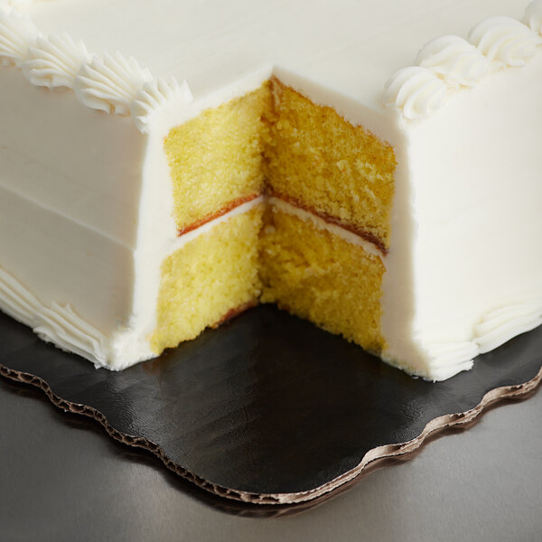 A black laminated Enjay sheet cake board under a white cake with a slice cut out.