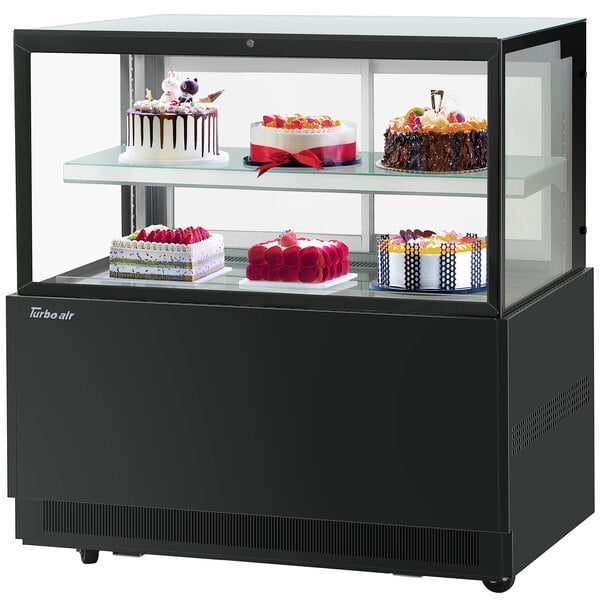 A Turbo-Air black refrigerated bakery display case with cakes on two tiers inside.