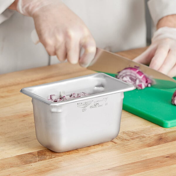 A person cutting onions in a Vollrath stainless steel hotel pan with a knife.