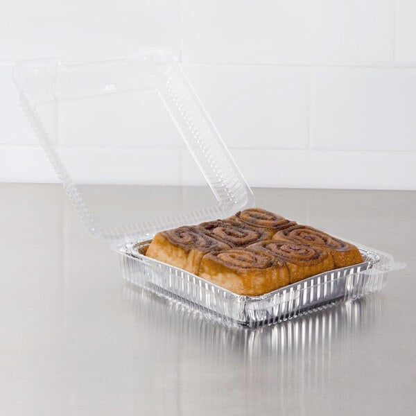 A cinnamon roll in a Dart clear hinged plastic container on a bakery counter.