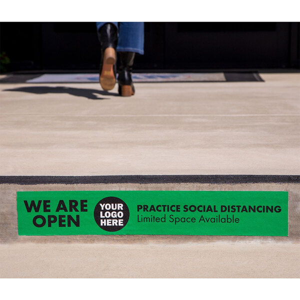 A person walking on a sidewalk with a green rectangular sign that says "We Are Open" on it.