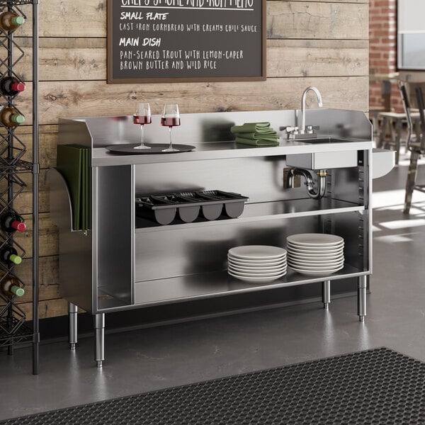 A stainless steel bussing and waitress station with a pan holder, sink bowl, and open shelving for plates and supplies.