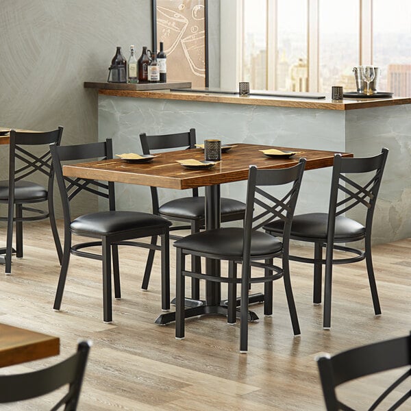 A Lancaster Table & Seating rectangular wood butcher block table with black chairs in a restaurant.