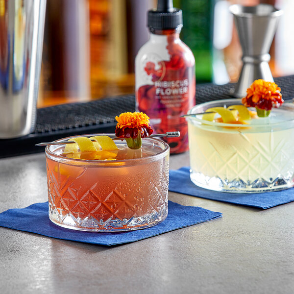 Two glasses of drinks with Wild Hibiscus flowers in them on a table.