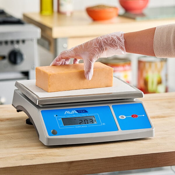 A person weighing a block of cheese on a blue and white AvaWeigh digital portion scale.