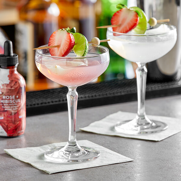 A bottle of Wild Hibiscus Rose and Hibiscus Floral Extract on a counter with two glasses of pink and white drinks.