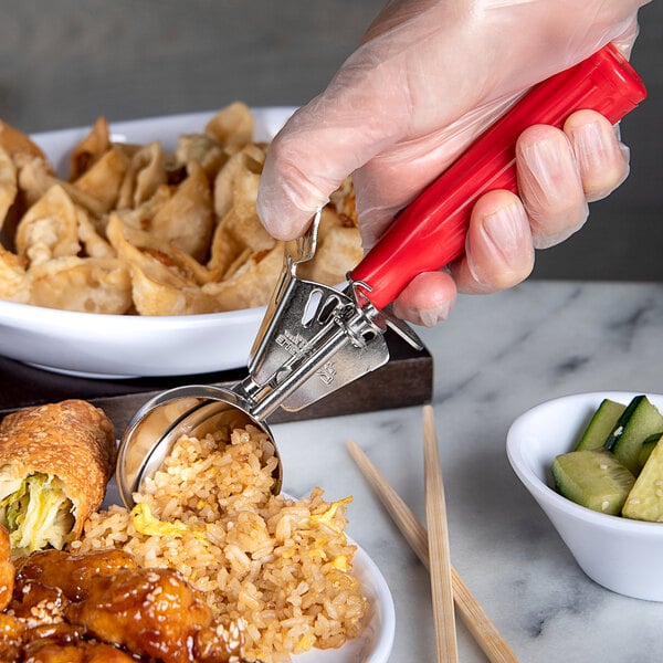 A hand holding a Carlisle red #24 thumb press scoop over a bowl of food.