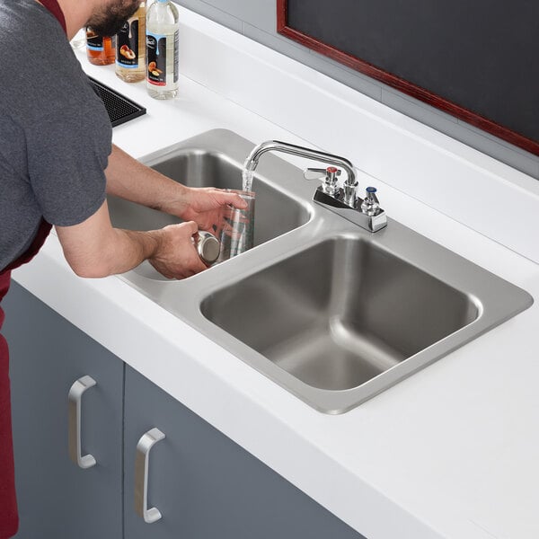 A man washing dishes in a Regency stainless steel drop-in sink with two compartments.