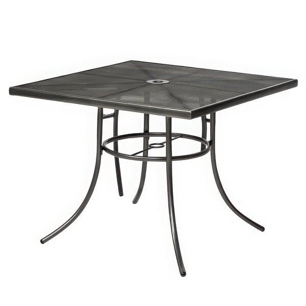 A rectangular black metal mesh table with a hole in the center on an outdoor patio.