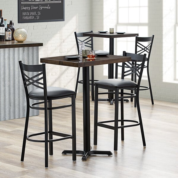 A Lancaster Table & Seating bar height butcher block table with two black chairs with cushions.