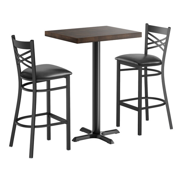 A bar height table set with a rectangular wood butcher block top and two black cross back chairs with cushioned seats.