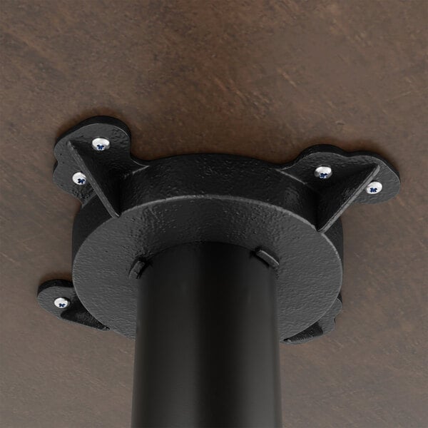 A black metal table base mounted to a wooden surface, part of a bar height table set.