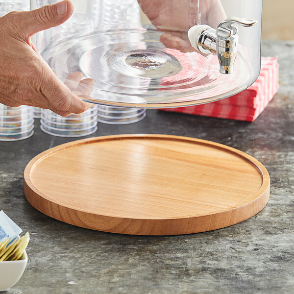 A hand holding a glass container with a spigot on a wood base.