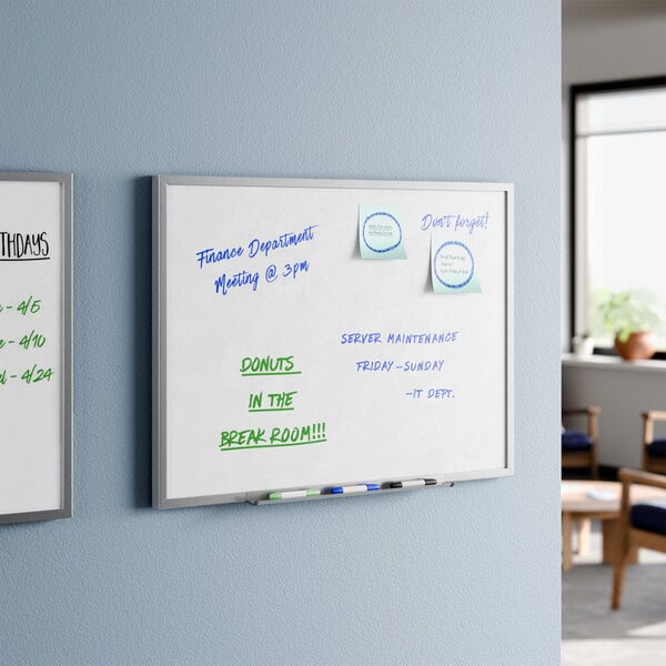 A wall-mounted 24 by 18 inch melamine whiteboard with an aluminum frame, shown with dry erase markers and notes written on it.