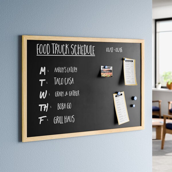 A rectangular black wall-mount magnetic chalkboard with a light wood frame.