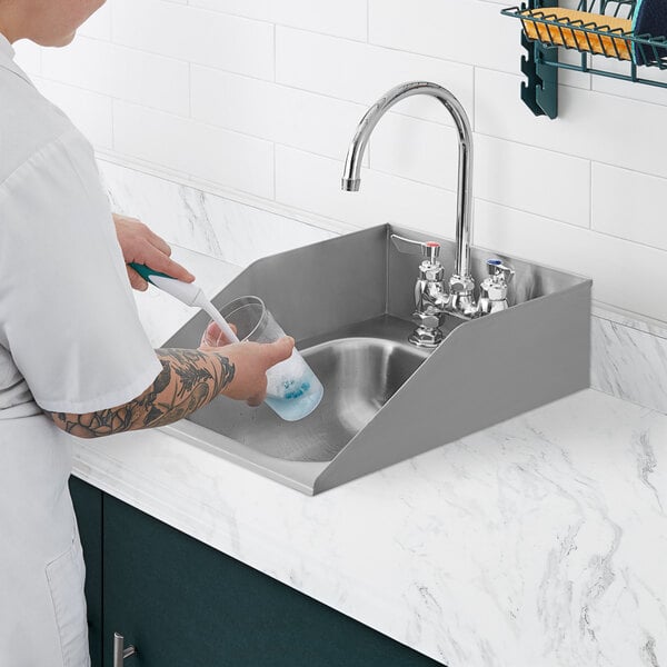 A person washing dishes in a Waterloo stainless steel drop-in sink.