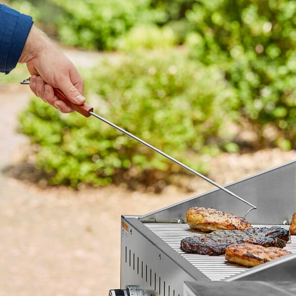 A person using an Outset meat hook to turn meat on a grill.