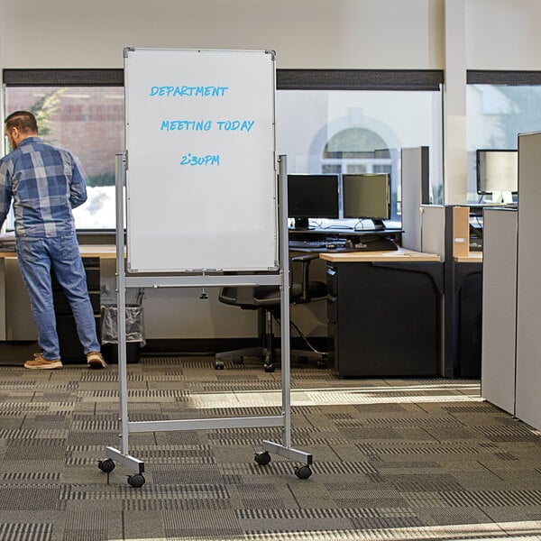 A man standing in an office using a Dynamic by 360 Office Furniture mobile whiteboard.