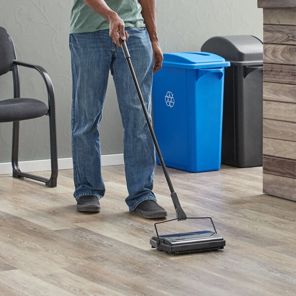 A man using a Lavex triple brush floor sweeper to clean the floor in a professional kitchen.