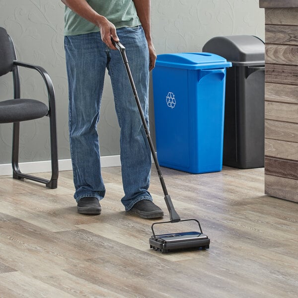 A person using a Lavex single brush floor sweeper in a professional kitchen.