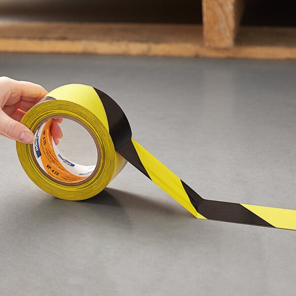 A hand holding a roll of Shurtape yellow and black warning stripe tape.