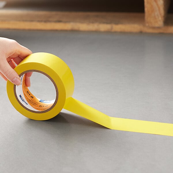 A hand holds a roll of Shurtape yellow line set tape.