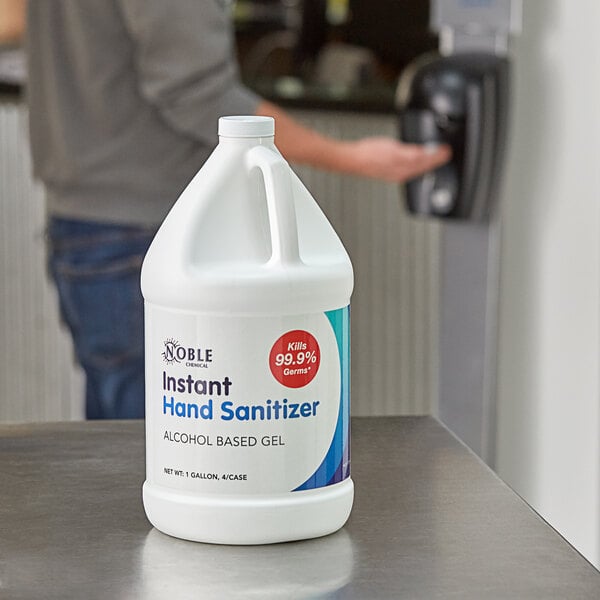 A man holding a white jug of Noble Chemical alcohol sanitizer with a blue and white label.