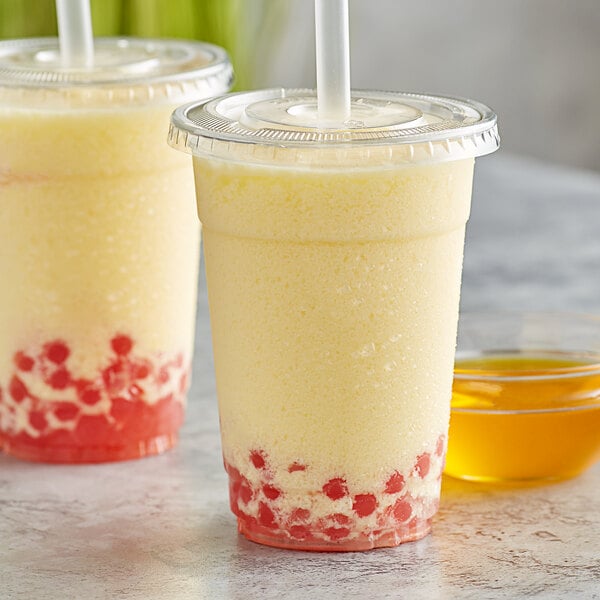 A close-up of a yellow drink in a plastic cup with a straw.