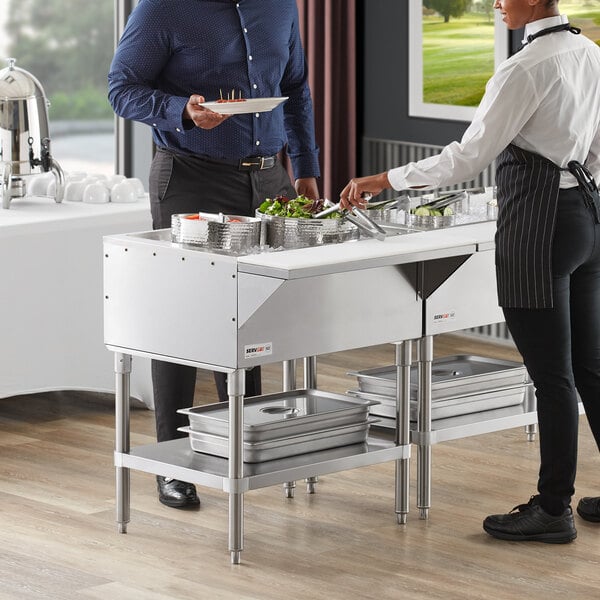 A man and woman standing in front of a ServIt cold food table on a hotel buffet.