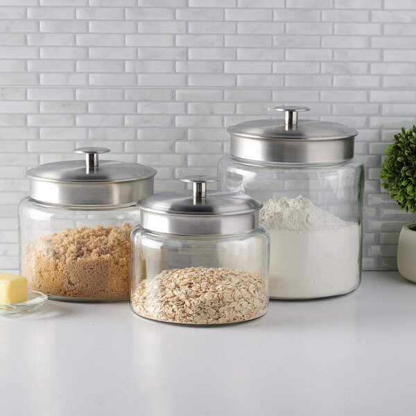 A set of clear glass storage jars with brushed metal lids, containing various dry ingredients.