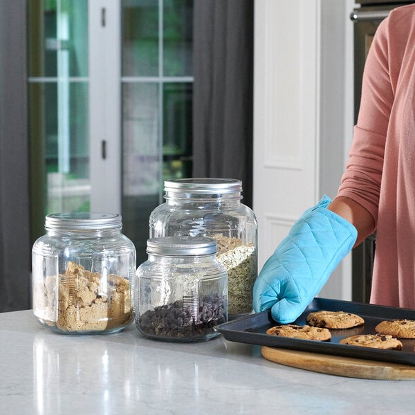 A 1-gallon glass cracker jar with a brushed metal lid, shown on a kitchen counter filled with baking ingredients.