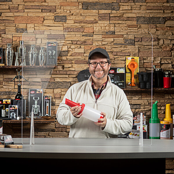A man standing behind a Tablecraft clear acrylic countertop safety shield on a convenience store counter.