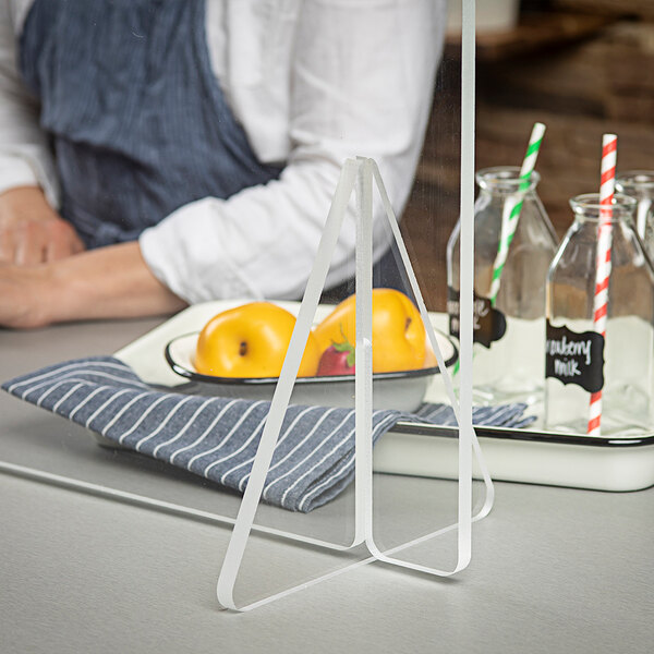 A woman using a clear acrylic freestanding countertop safety shield at a hospital cafeteria table with a glass of juice and a bottle of milk with a straw.