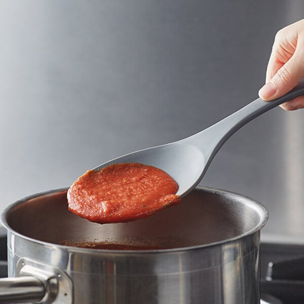 A person holding a Tablecraft flexible silicone spoon over a pot of red sauce.